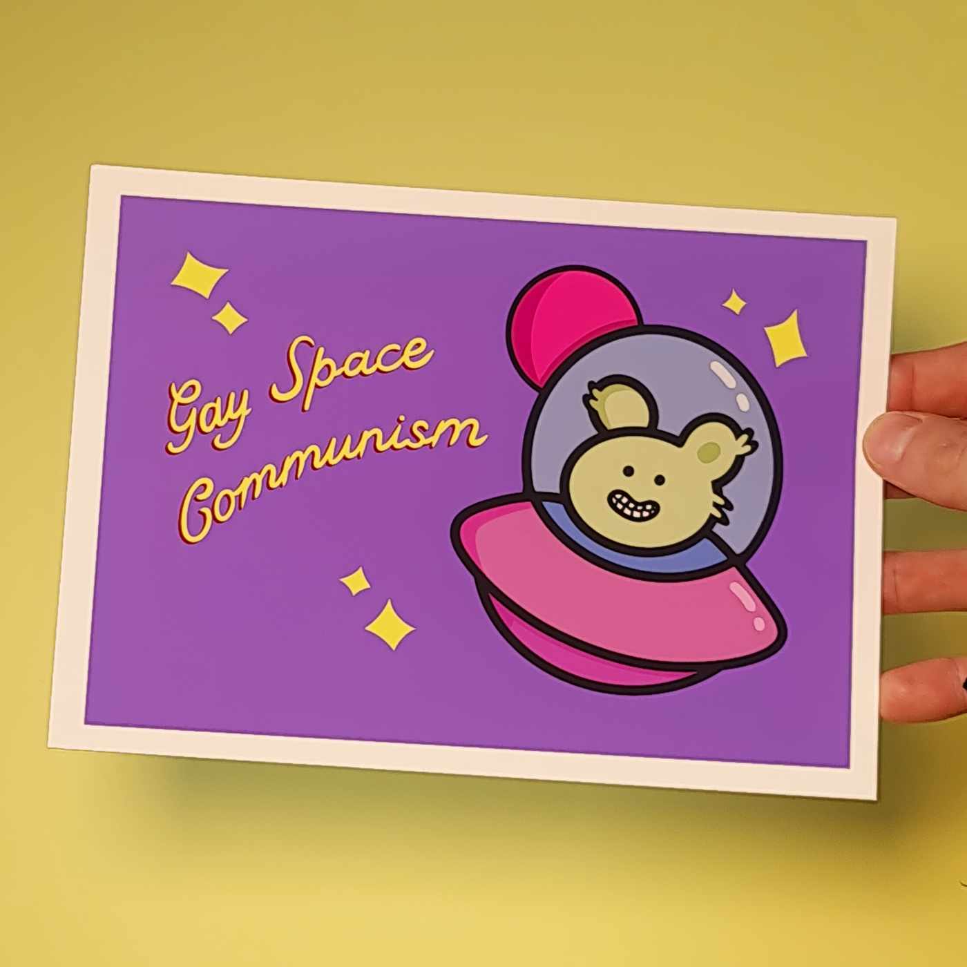 Eläin virnuilee lentävässä lautasessa, taustalla planeetta. Teksti Gay Space Communism
